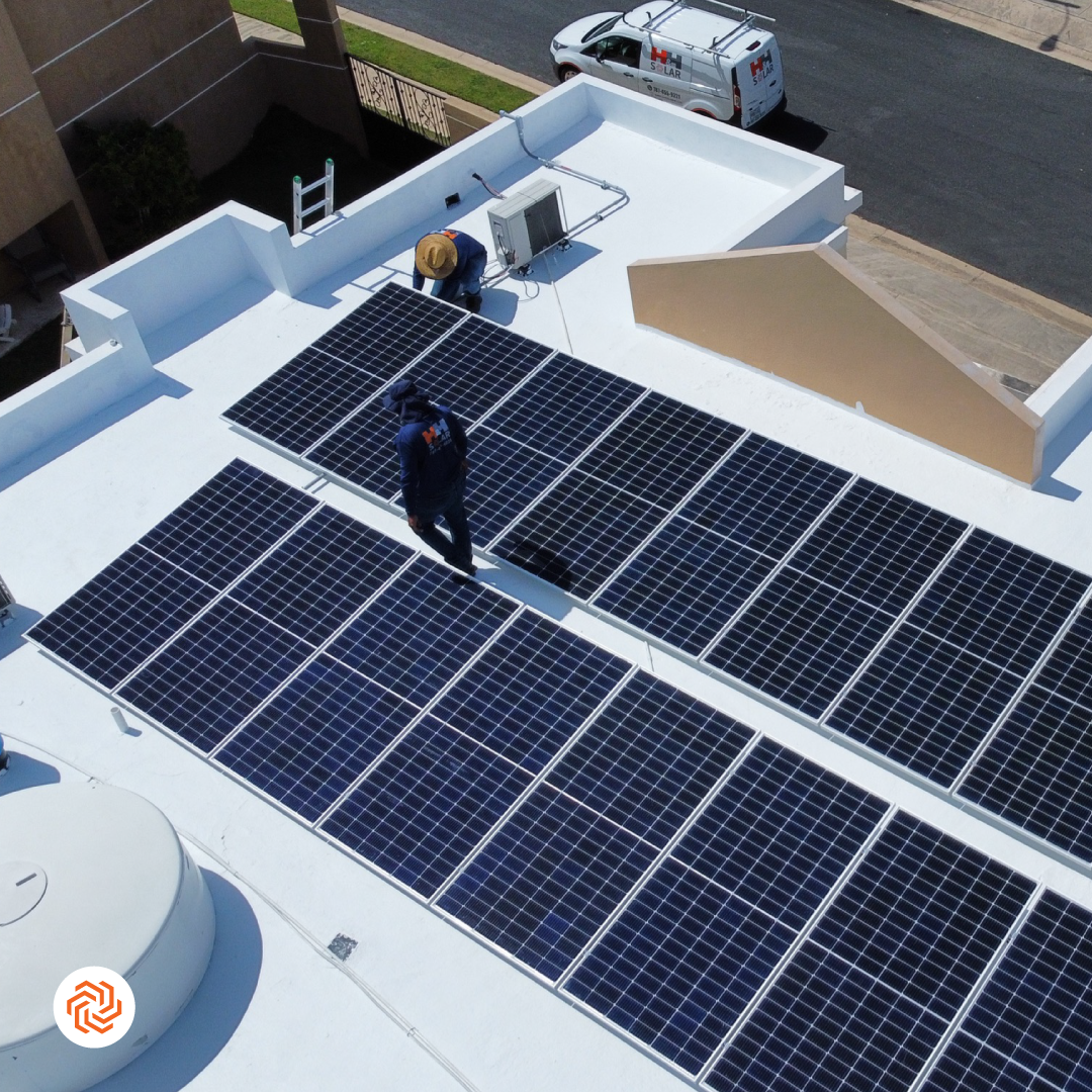 Familia latinx de cuatro personas sonriente en el patio con paneles solares en el techo visible al fondo, luz de tarde cálida, estilo fotográfico realista que transmite seguridad y ahorro familiar.