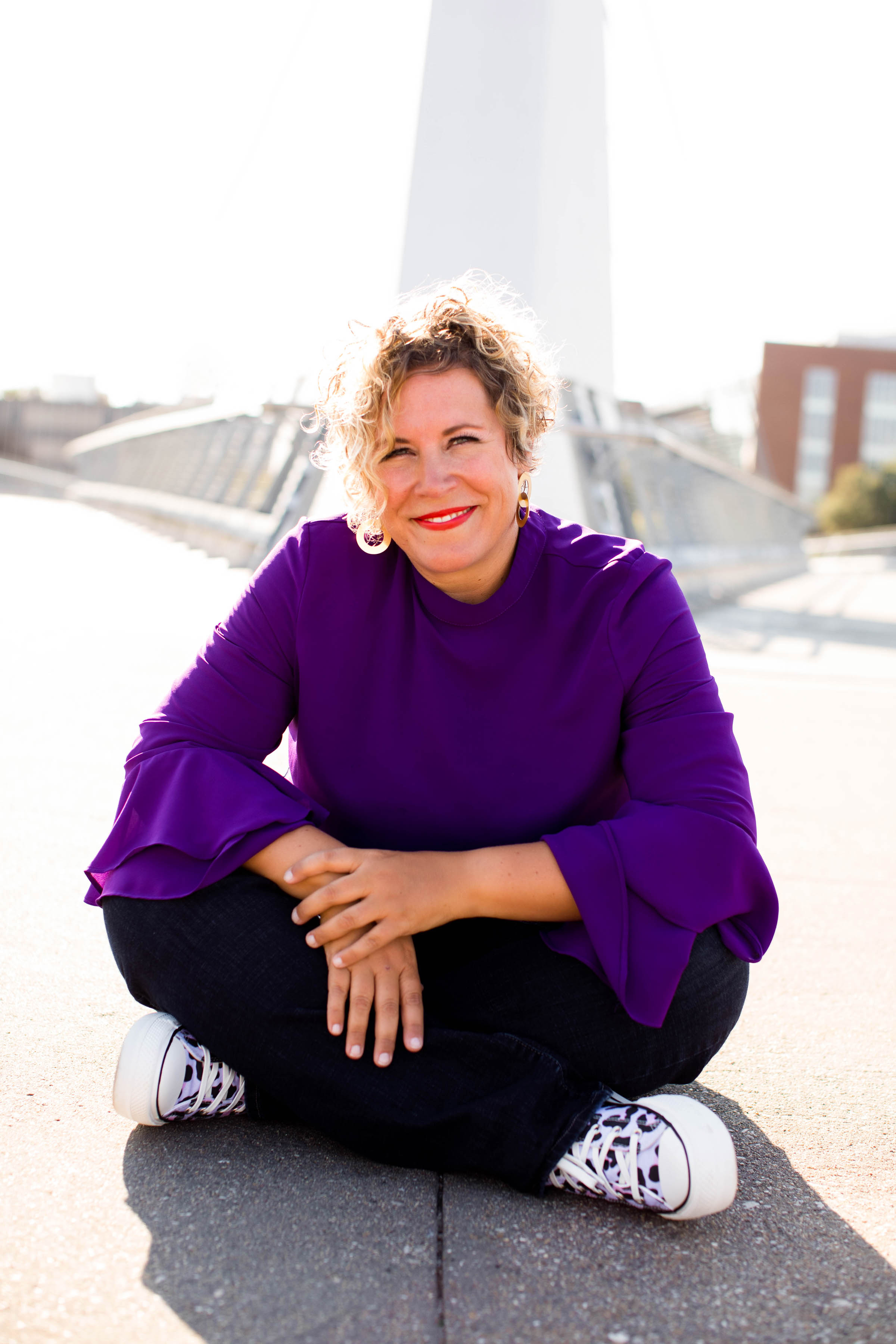 Wendi Fredregill seated on a bridge in Des Moines, wearing a purple shirt and purple leopard-print Converse