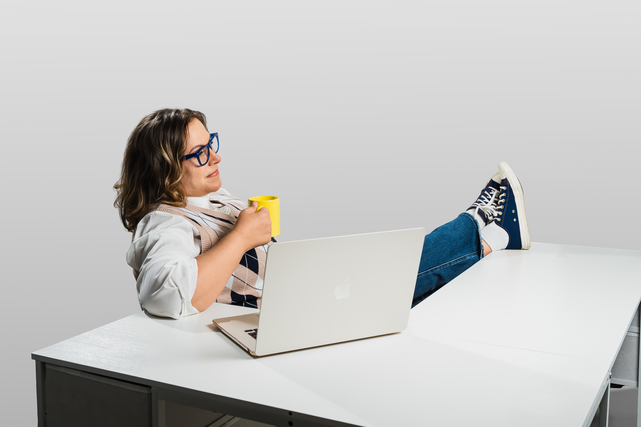 Wendi leaning back with feet up on the desk, holding a mug