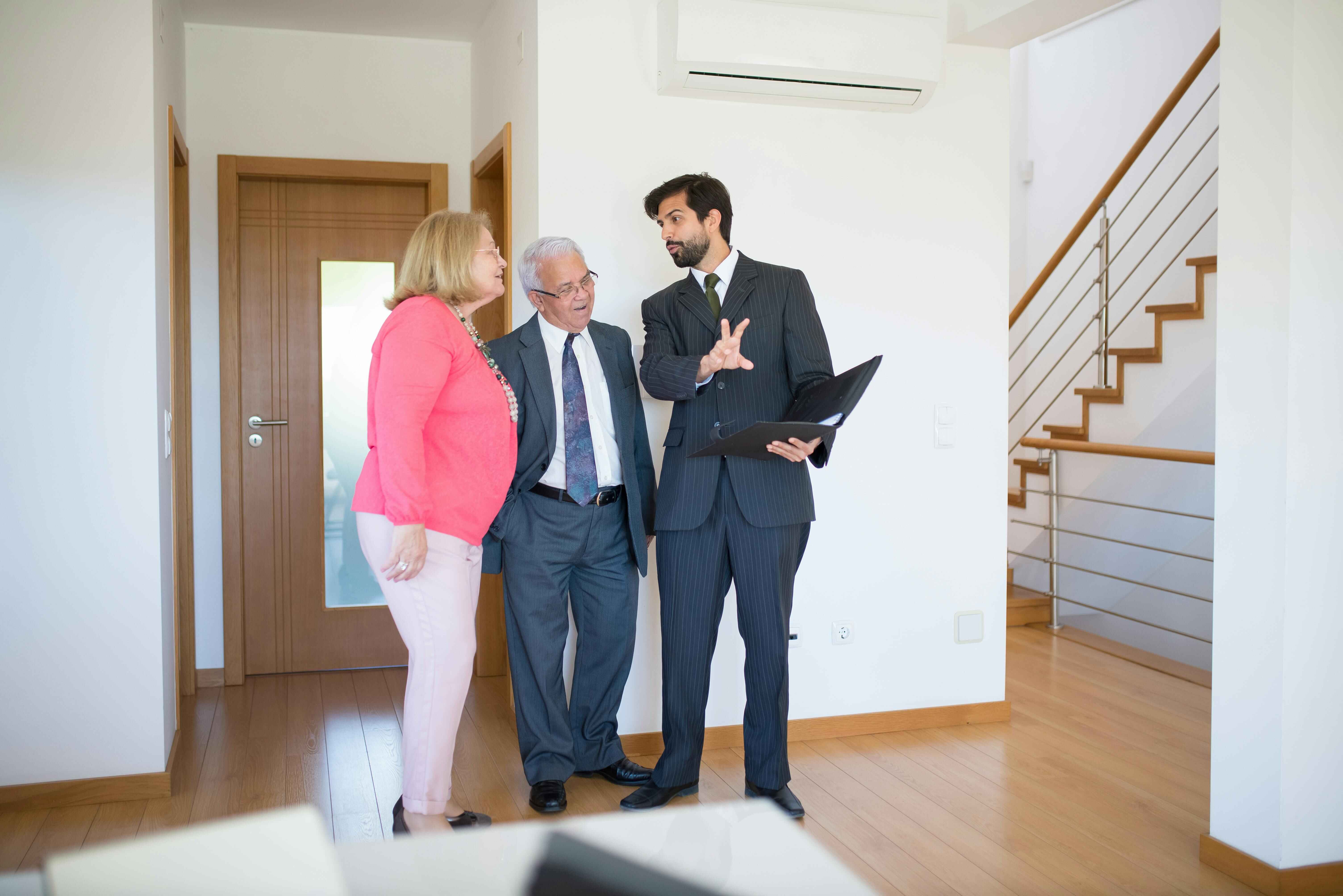 Real estate agent explaining property details to an elderly couple inside a modern home during a house viewing. Real estate agent explaining property details to an elderly couple inside a modern home during a house viewing.