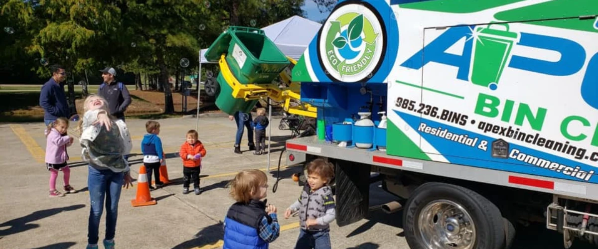 Community demonstration showing trash bin cleaning equipment in action with families watching.