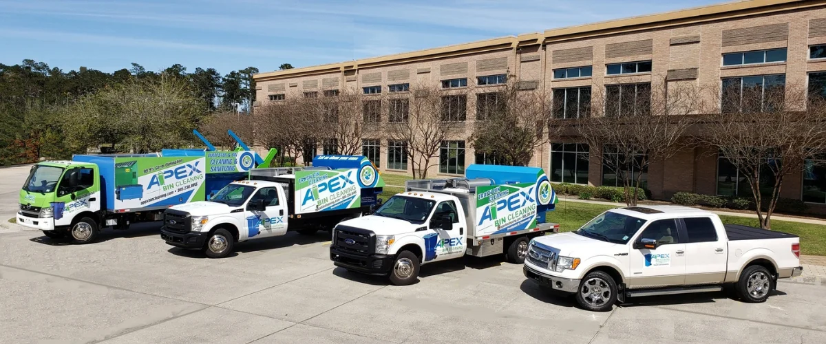A fleet of Apex Bin Cleaning trucks and a pickup truck parked in front of a modern brick office building.