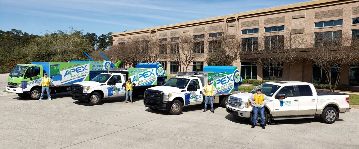Four Apex Bin Cleaning employees stand proudly in front of their company vehicles, including three specialized cleaning trucks and a pickup.