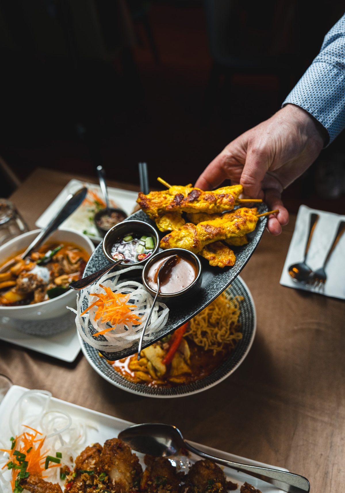 A plate of chicken satay skewers being served to the table