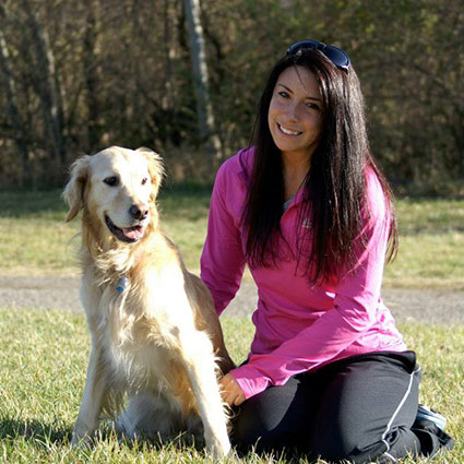 Young Woman with Long Dark Brown Hair and a Pink Blouse, Smiling While Sitting in the Grass next to a Golden Labrador Retriever.