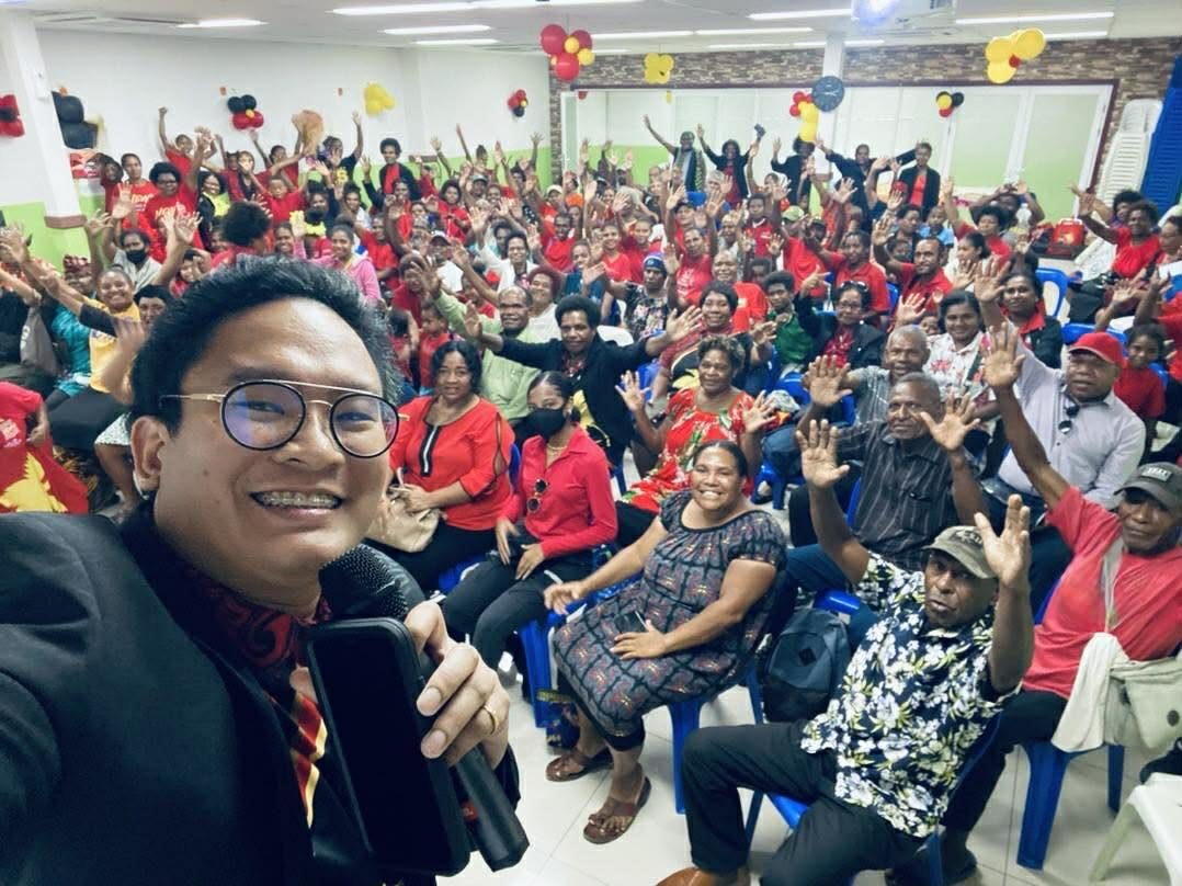 Coach Rojie Jardio at the front of a full room, the audience behind him with hands raised
