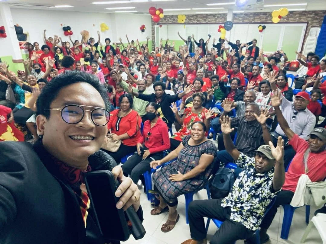 Mentor Rojie in front of a room, the audience behind him with hands raised