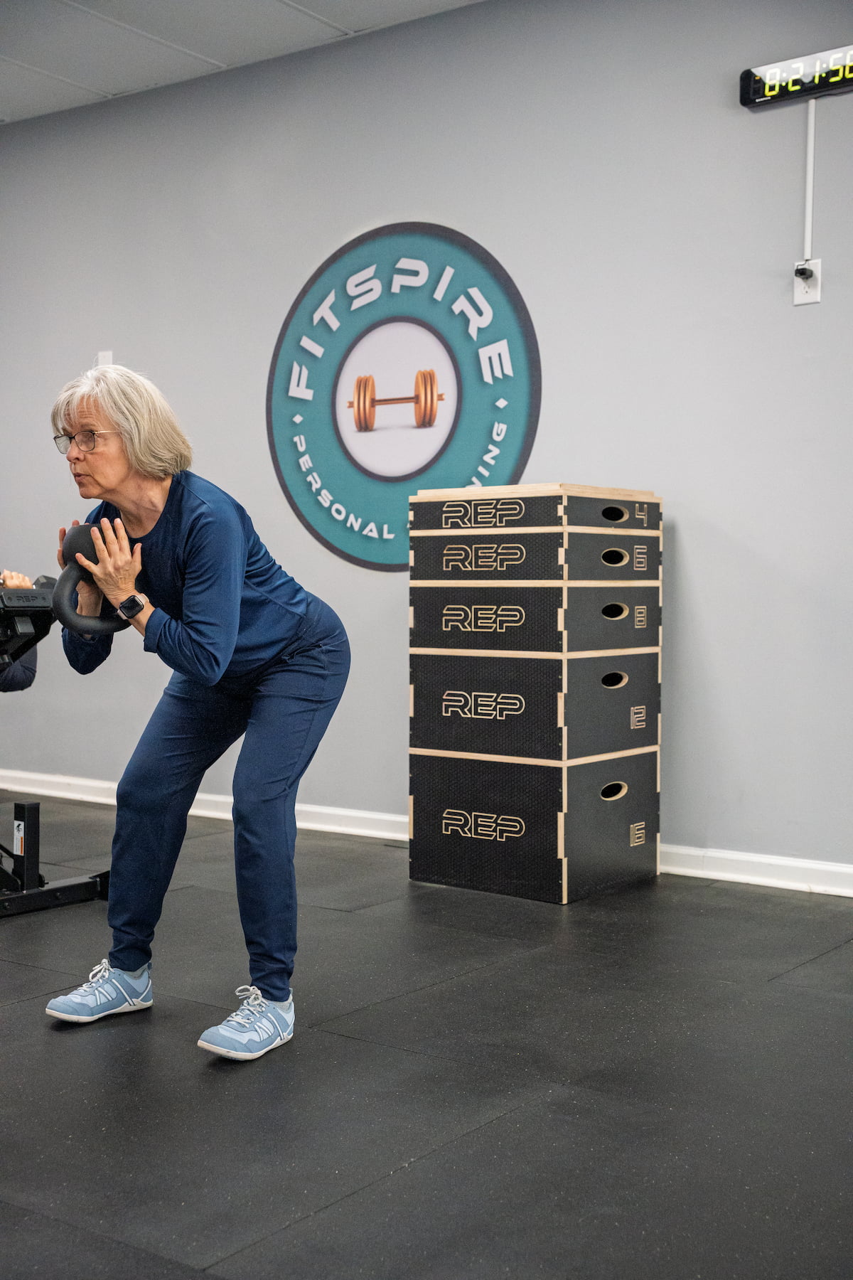 Fitspire member performing kettlebell exercise with Fitspire logo in background