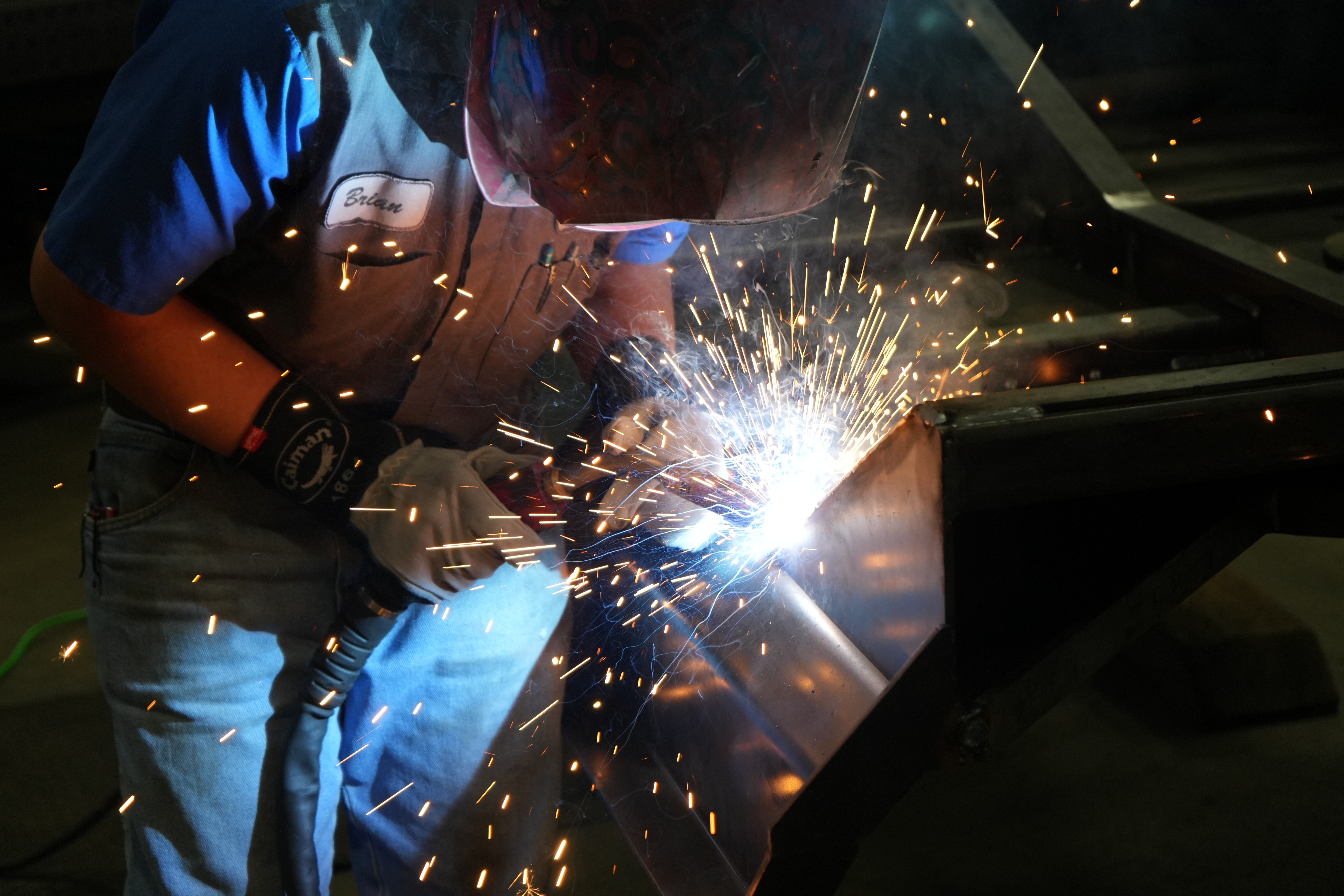 Craftsman welding a custom skid steer attachment in a metal fabrication workshop Craftsman welding a custom skid steer attachment in a metal fabrication workshop
