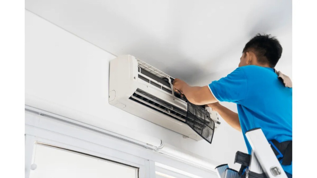 Technician cleaning a wall-mounted aircon filter on a ladder