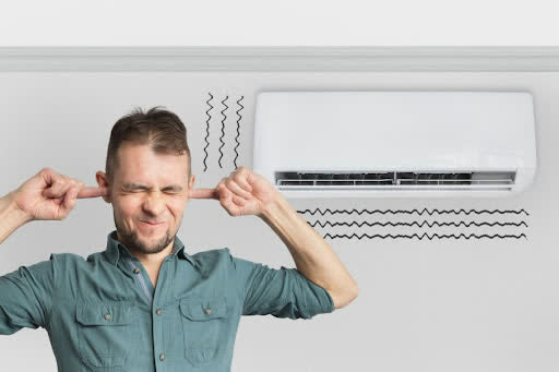 Man covering his ears next to a noisy wall-mounted air conditioner