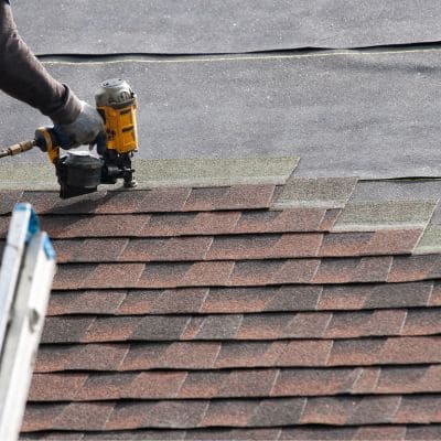 Roofer using a pneumatic nail gun during the installation of shingles