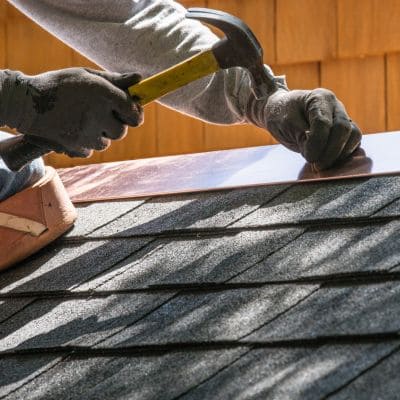 A roofer hammering down roofing components