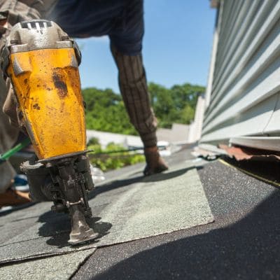 Professional roofer using a nail gun to install asphalt shingles