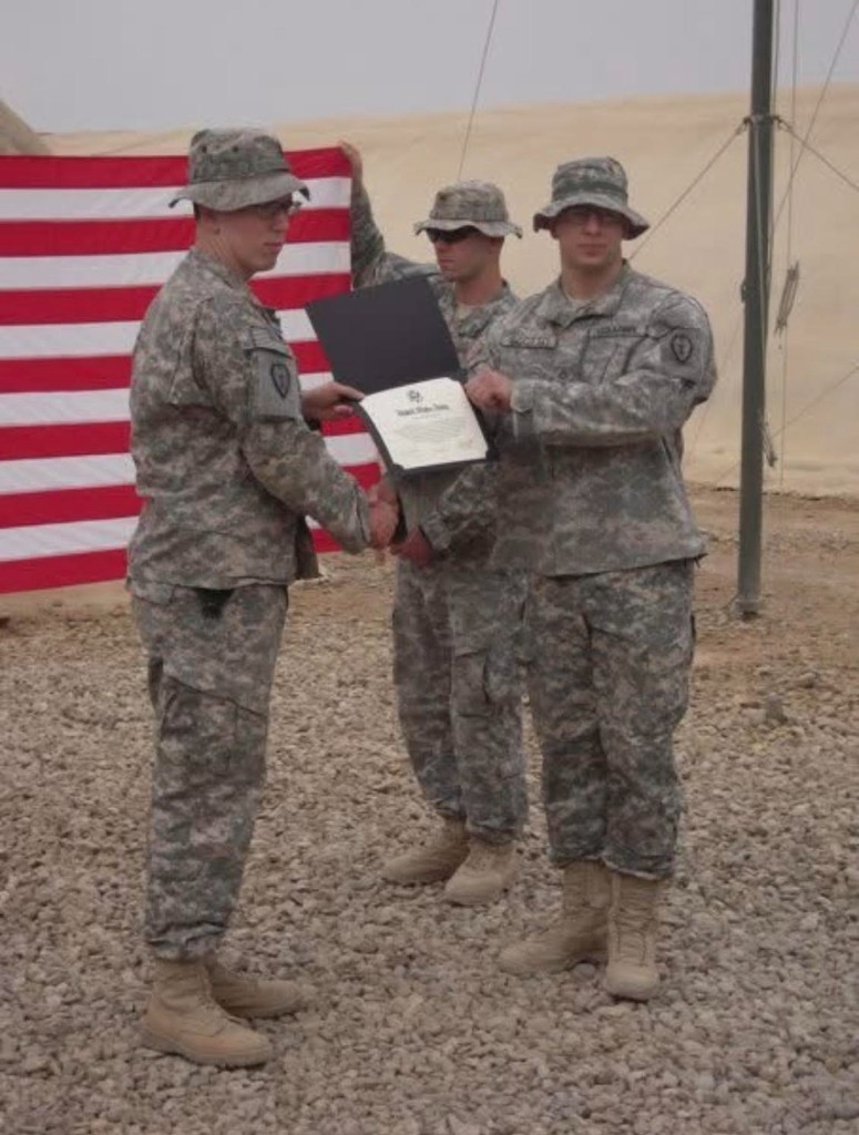 Jaren Scotto receiving recognition in front of an American flag, deployed to Iraq