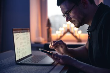 Man working late night on laptop and smartphone for digital marketing campaign - TSG Group New York