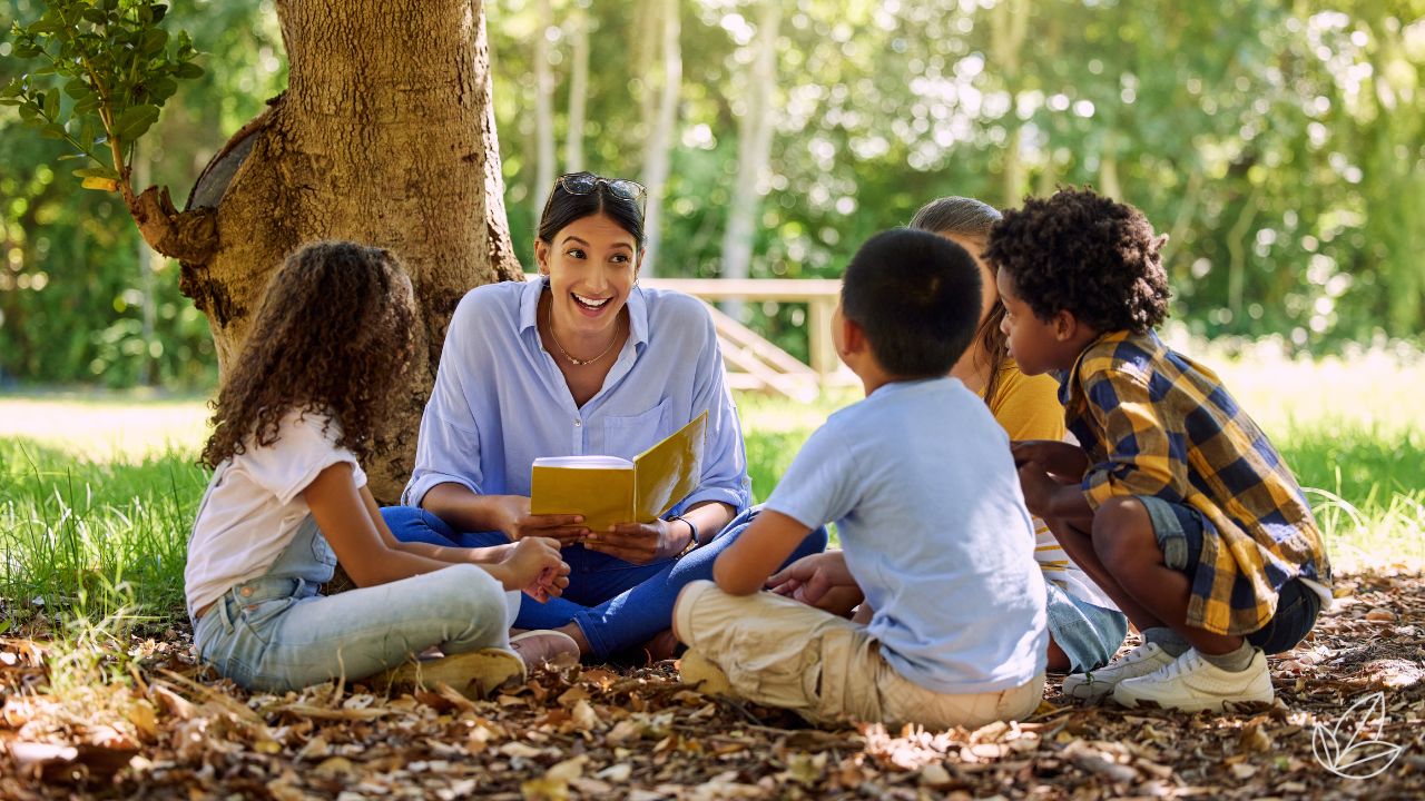 A teacher reading with children beneath a tree