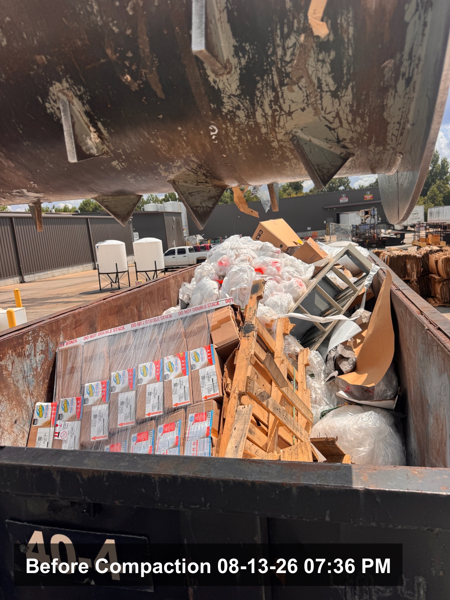 A mobile compaction unit working a packaging-heavy roll-off container between dock doors