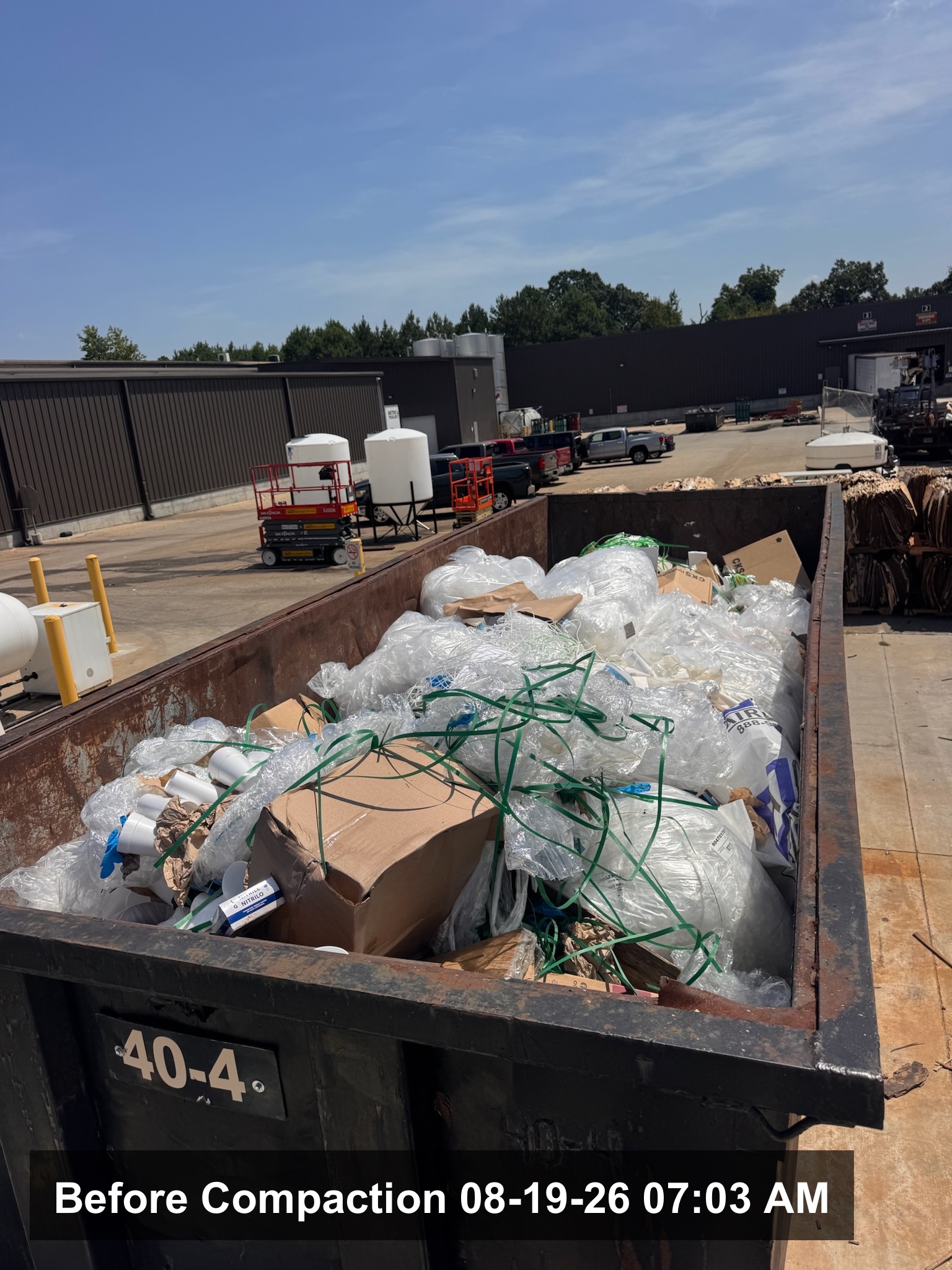 Service drive behind a strip center at opening time with the container pad swept clean in West Macon