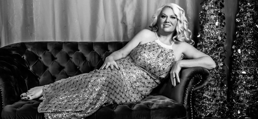Black and white photo of a woman in a sequined gown reclining on a velvet sofa.