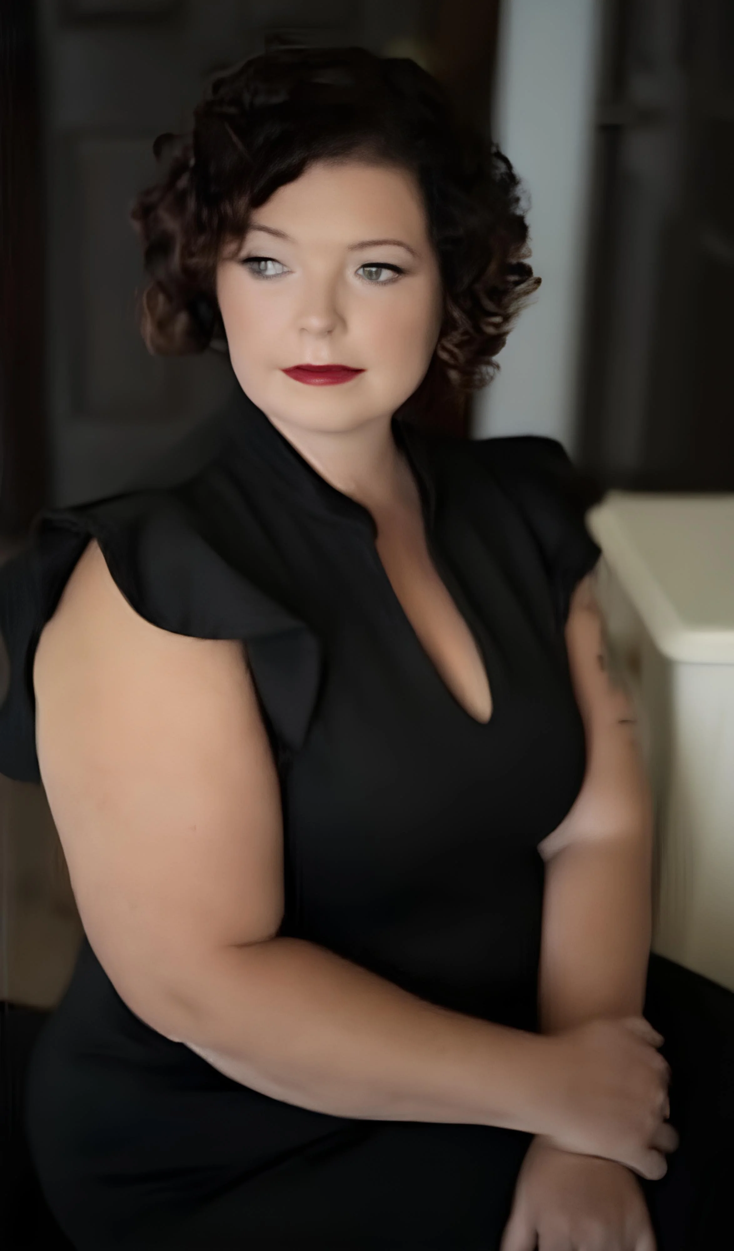 Woman with curly hair in black dress, sitting and looking to the side.