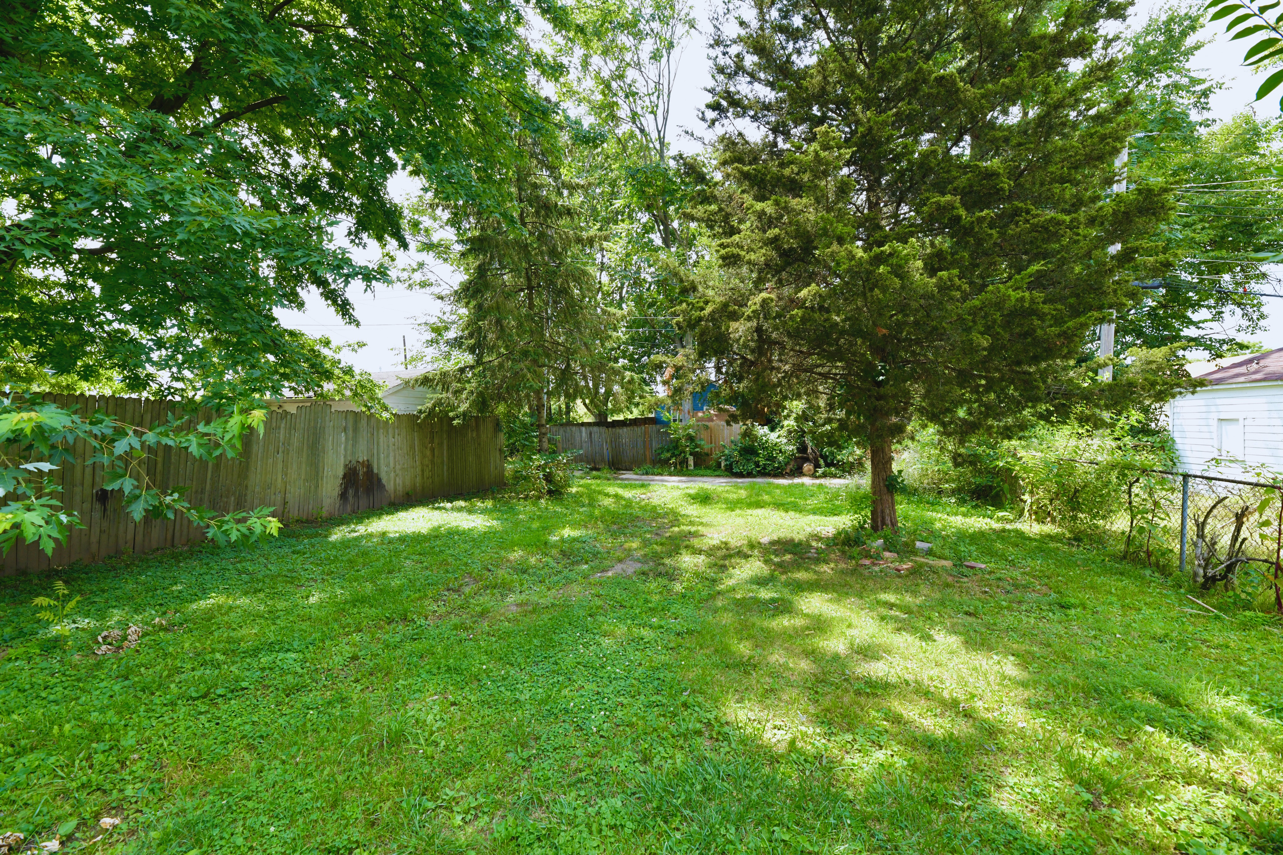 Vacant grassy residential lot in Indianapolis with mature trees, fencing, and nearby homes showing infill development potential Vacant grassy residential lot in Indianapolis with mature trees, fencing, and nearby homes showing infill development potential