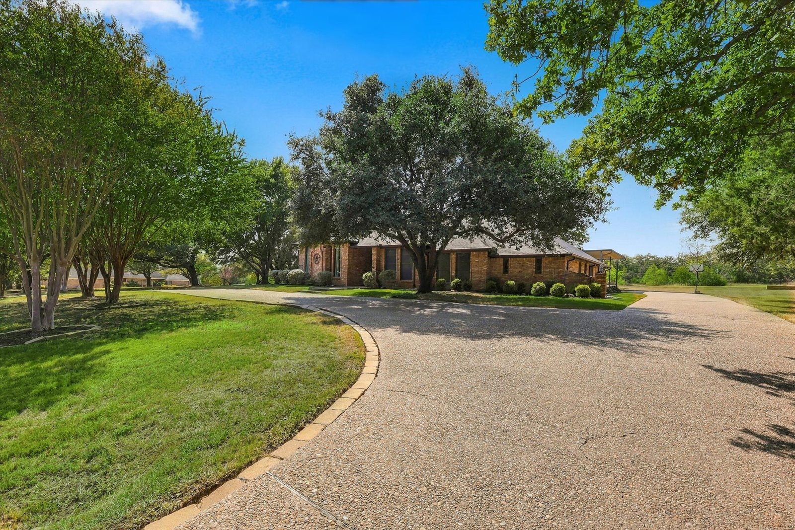 Flower Mound acreage home with a circle driveway, mature trees, and covered parking