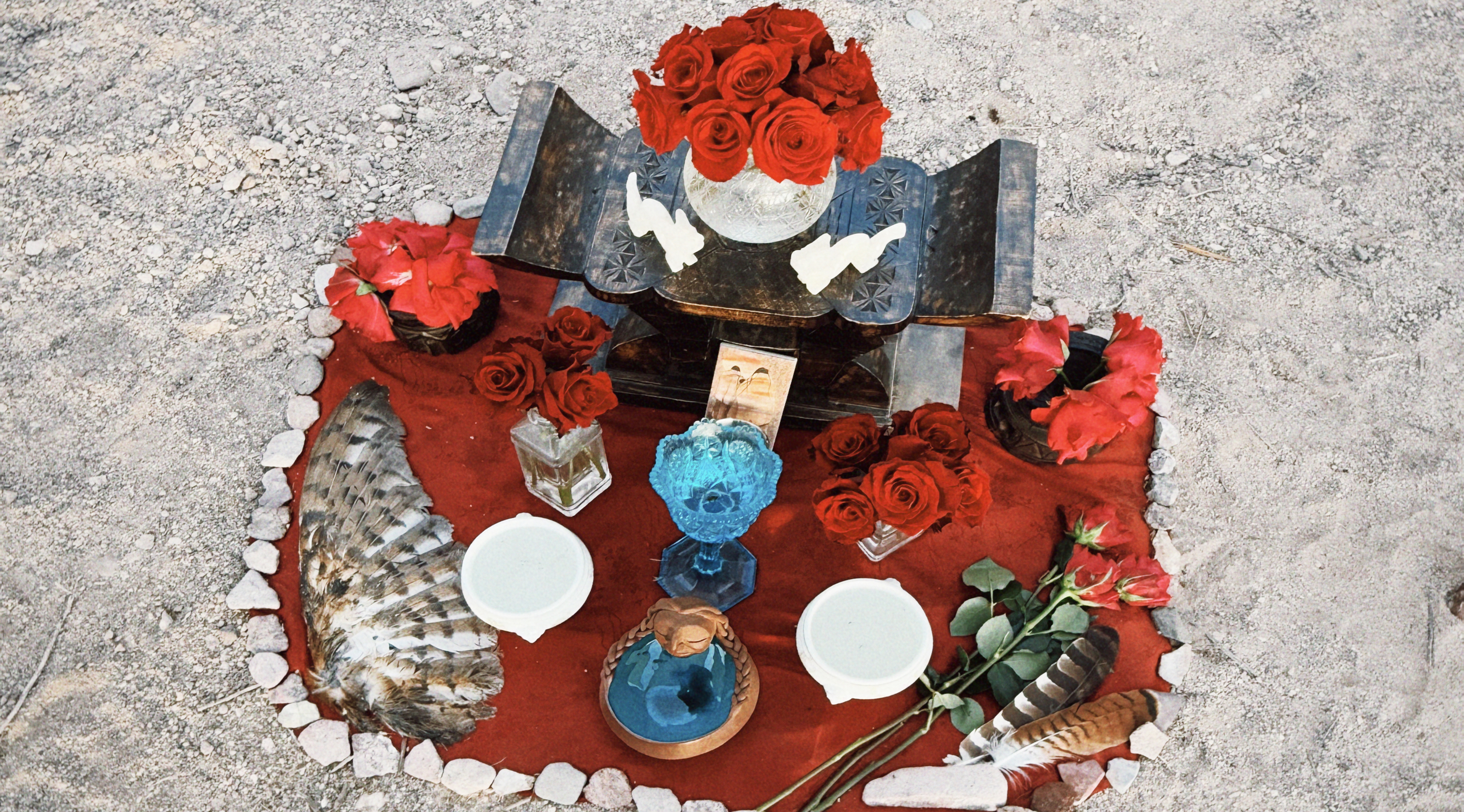 Rose altar with red roses, ceremonial vessels, and feathers