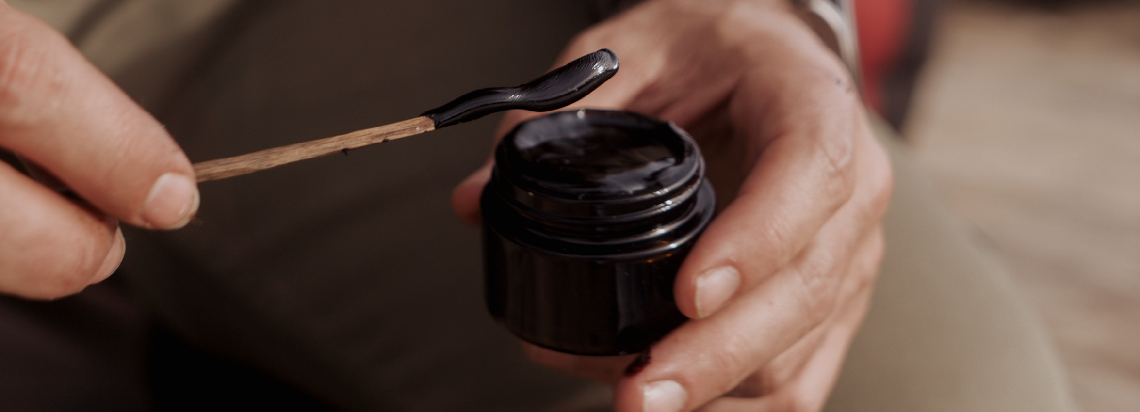 Hands holding a jar of Tobacco paste with a small wooden spoon