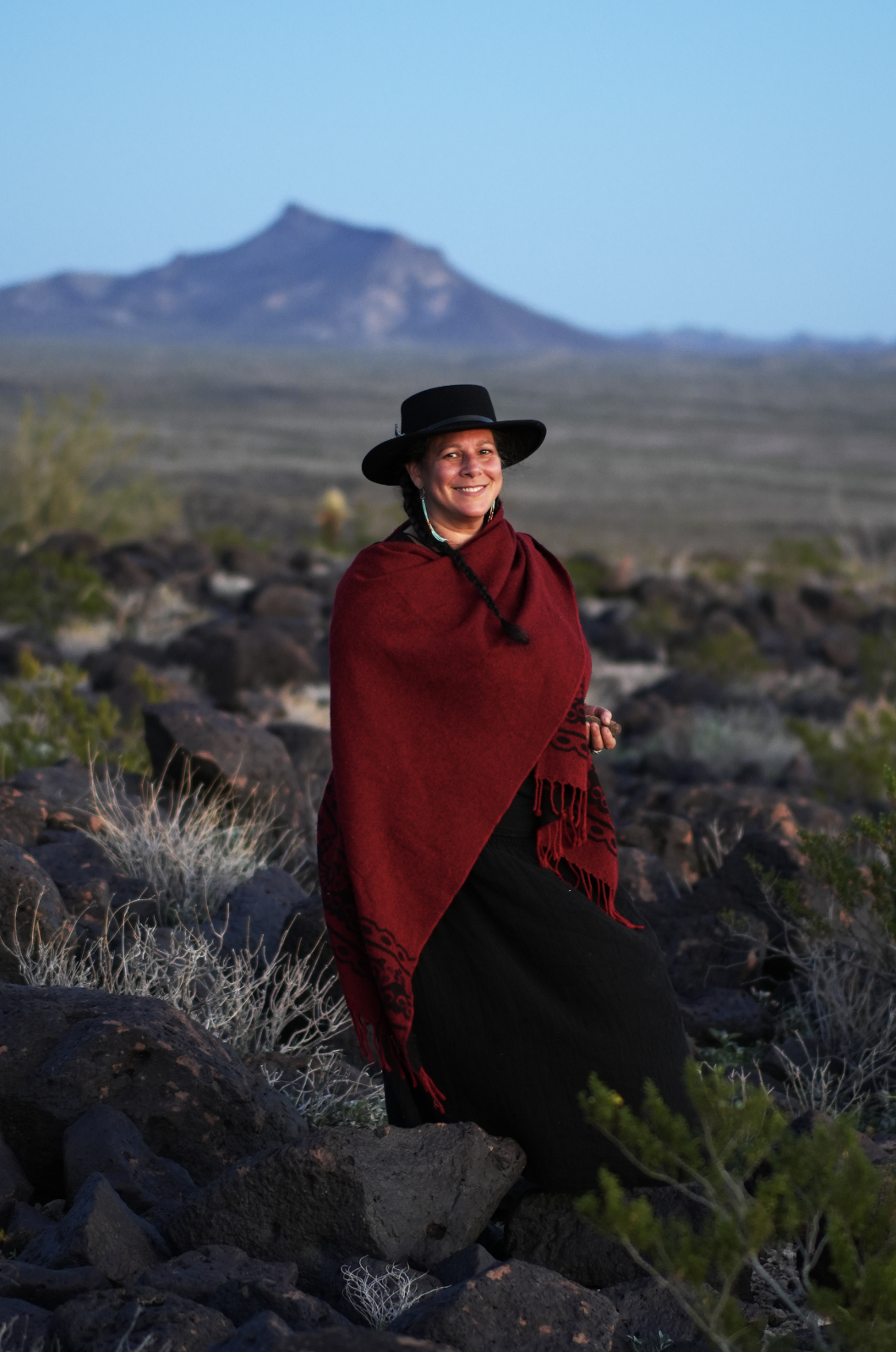 A participant in a red shawl and black hat in the desert