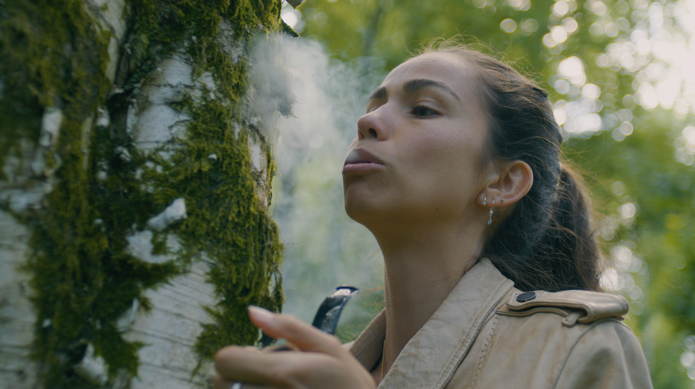 A practitioner working with pipe smoke beside a moss-covered tree