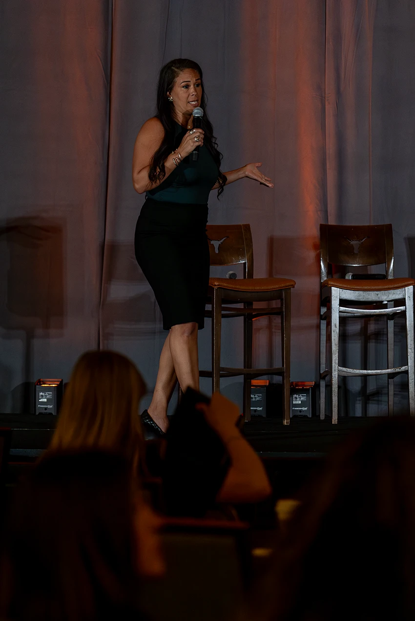 Cathy Christen speaking on stage with a handheld microphone