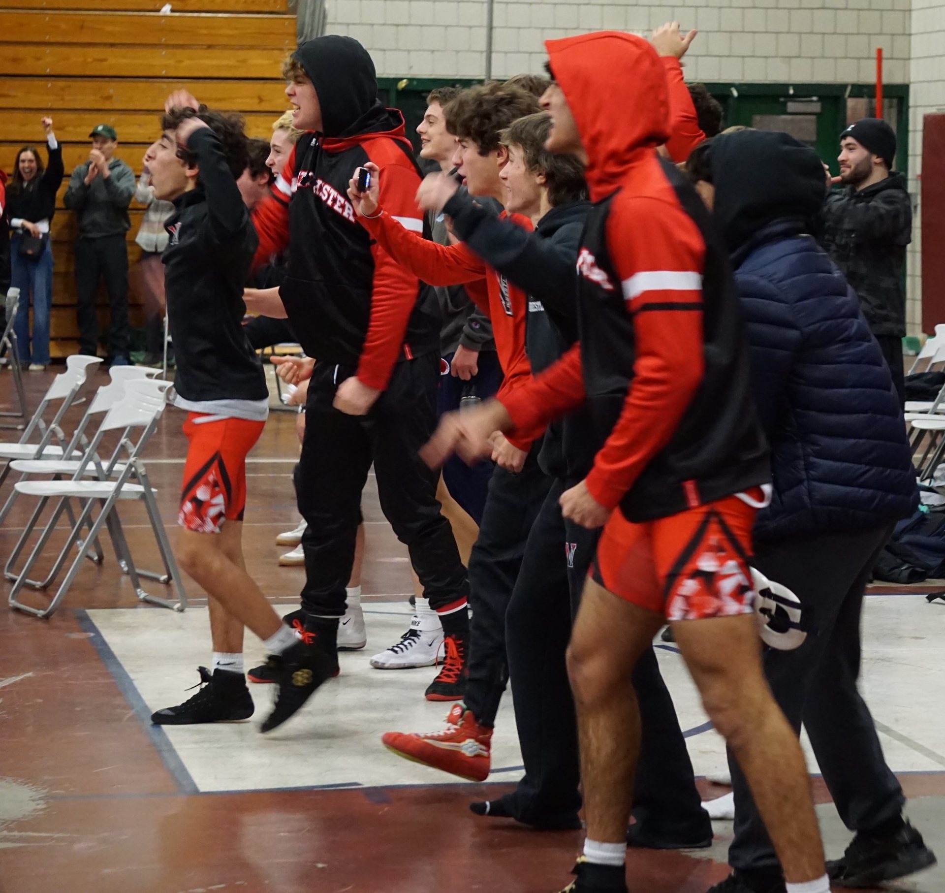 Winchester wrestlers on their feet cheering for a teammate during a match