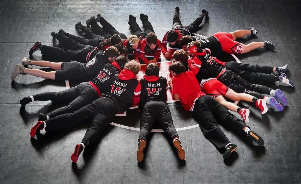 Winchester wrestlers lying in a circle on the mat, heads together at center