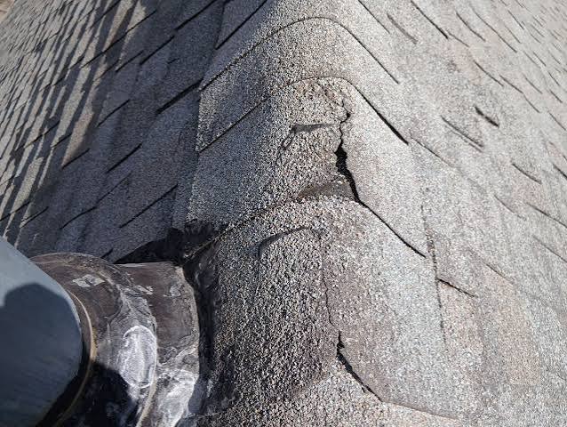 Cracked asphalt ridge shingles beside a roof vent