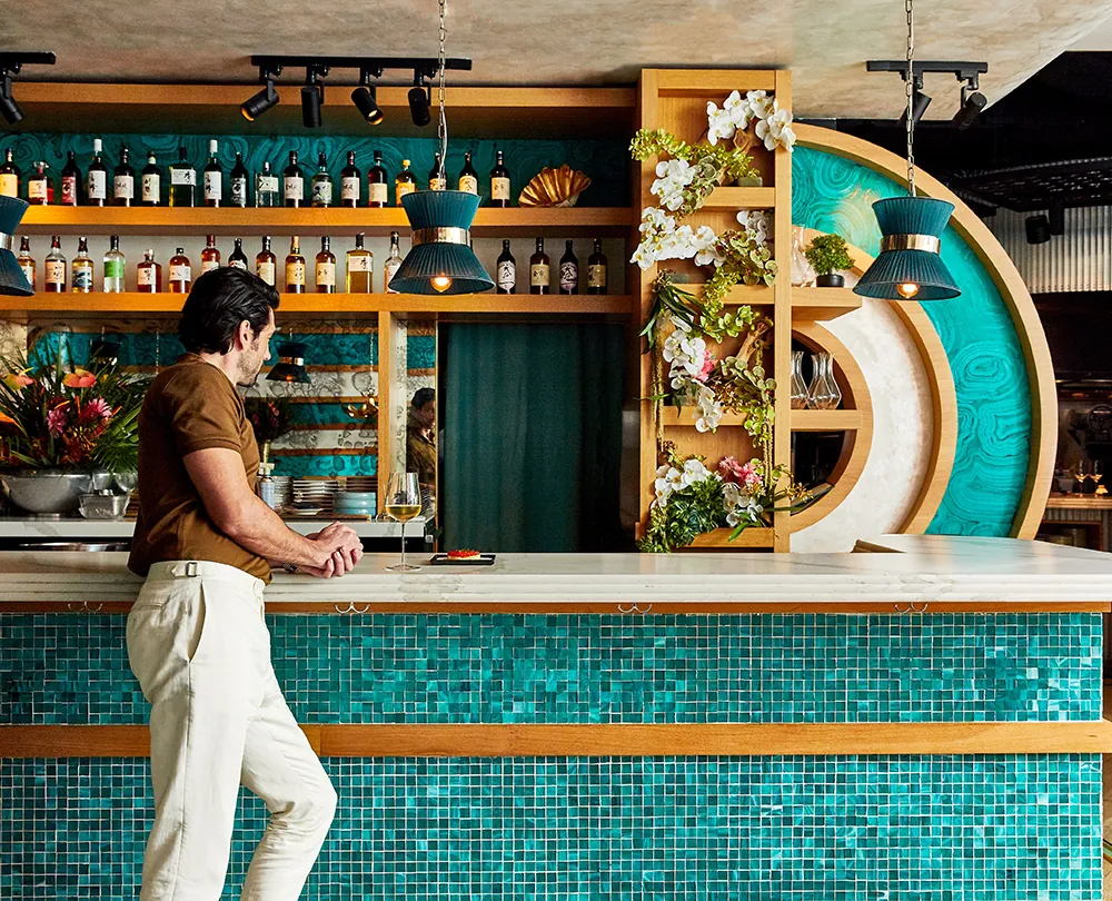 A bar with teal tile and a guest leaning on the counter