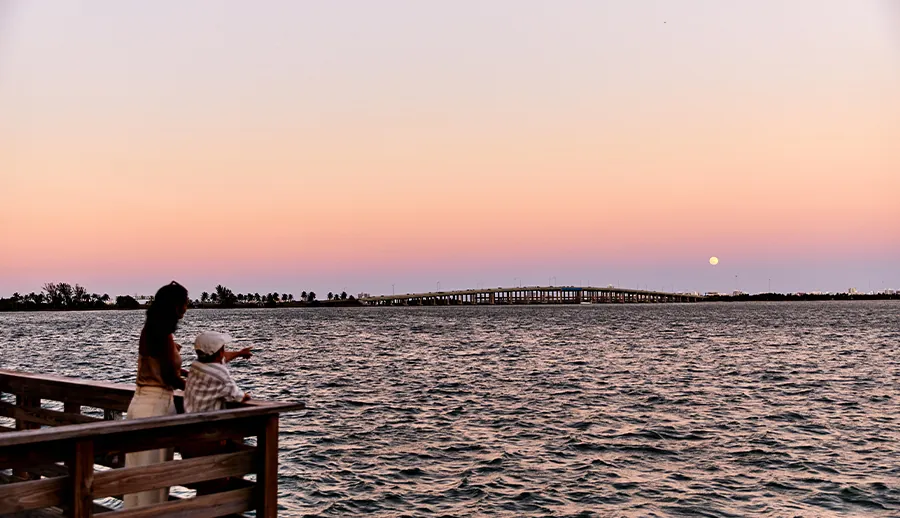 A person watching the sunset from a wooden pier on the bay