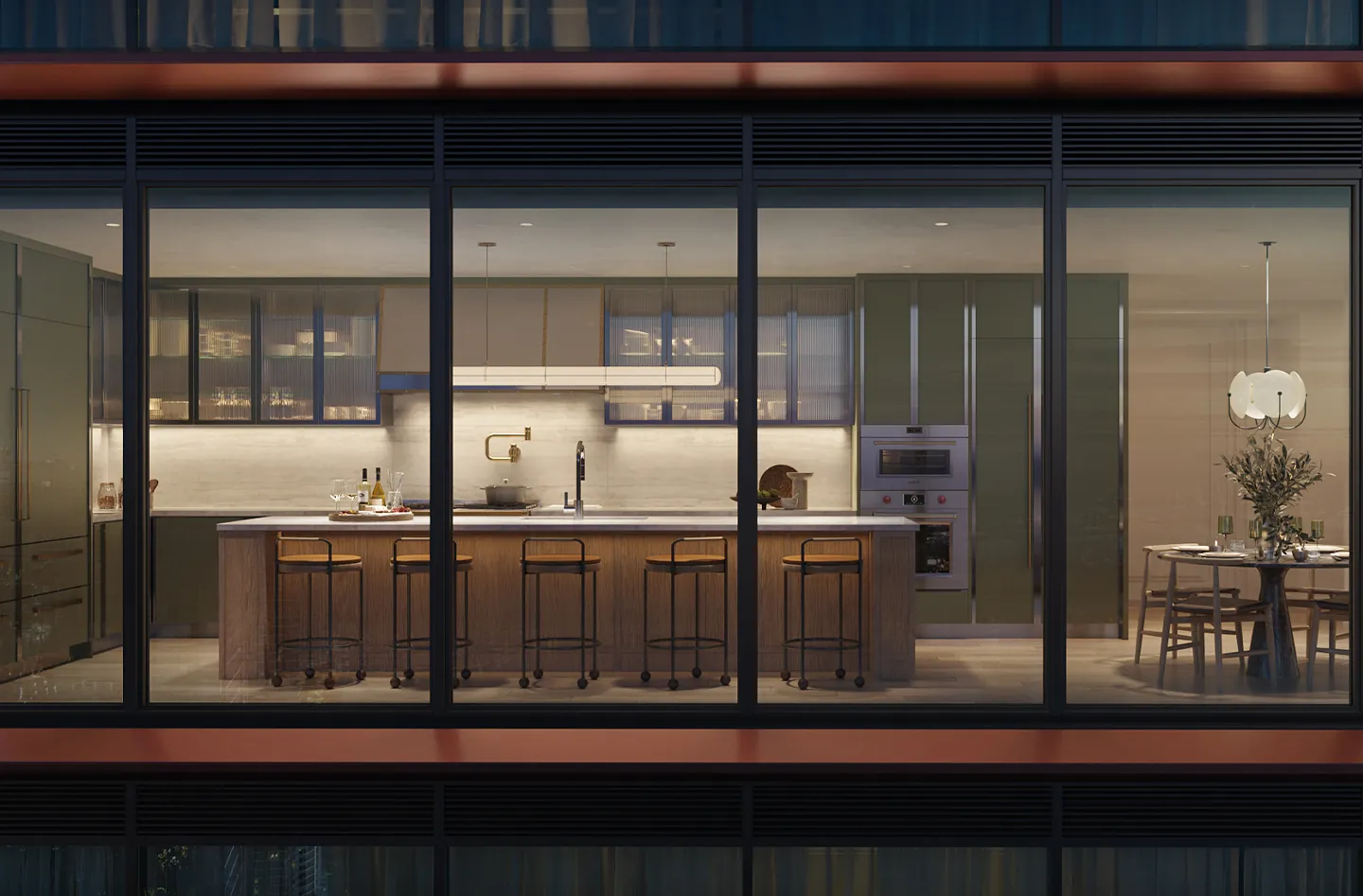 A lit kitchen with a long island seen through a copper-framed glass facade at night