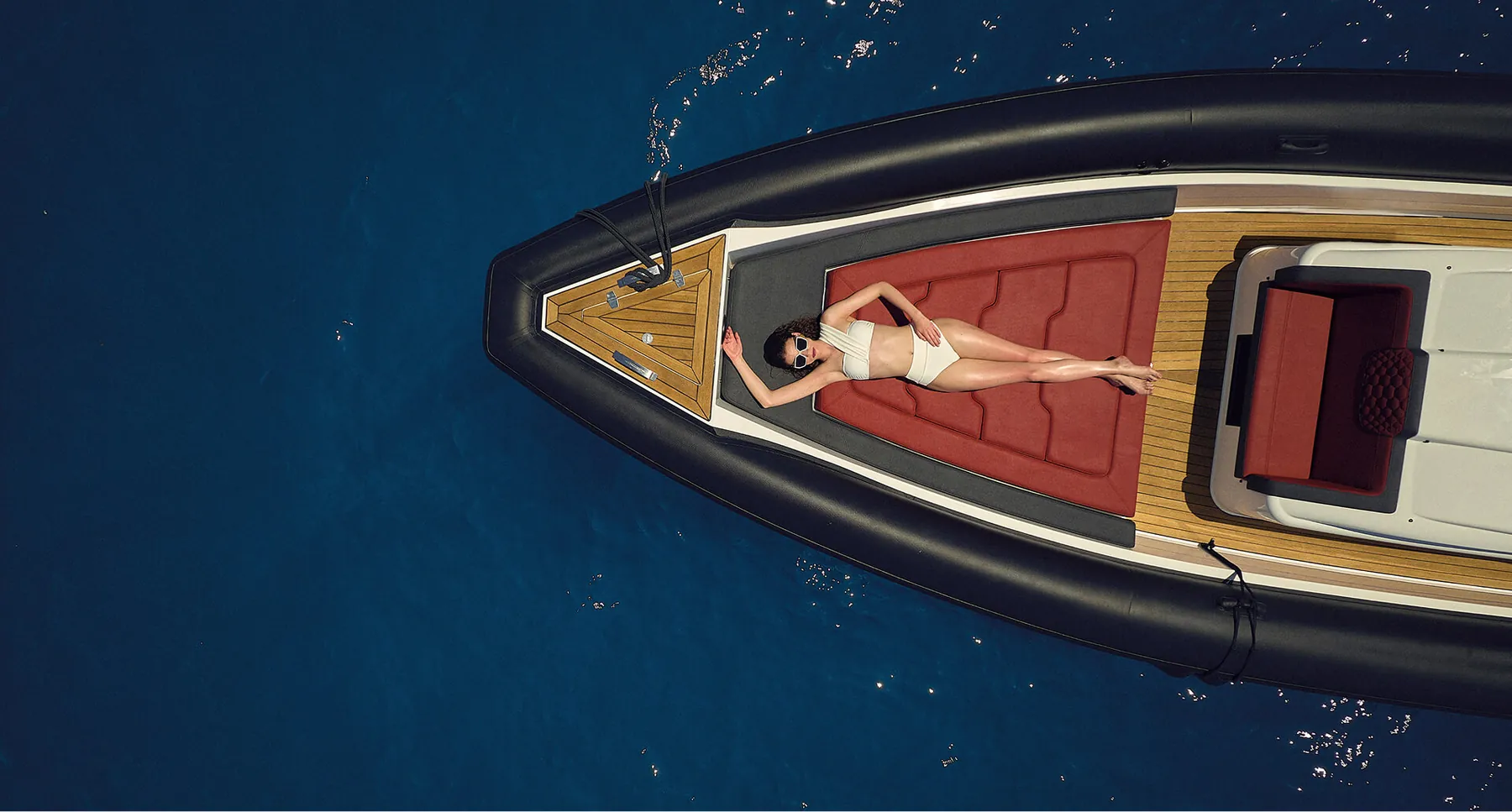 Aerial view of a person lying on the deck of a wooden boat on deep blue water