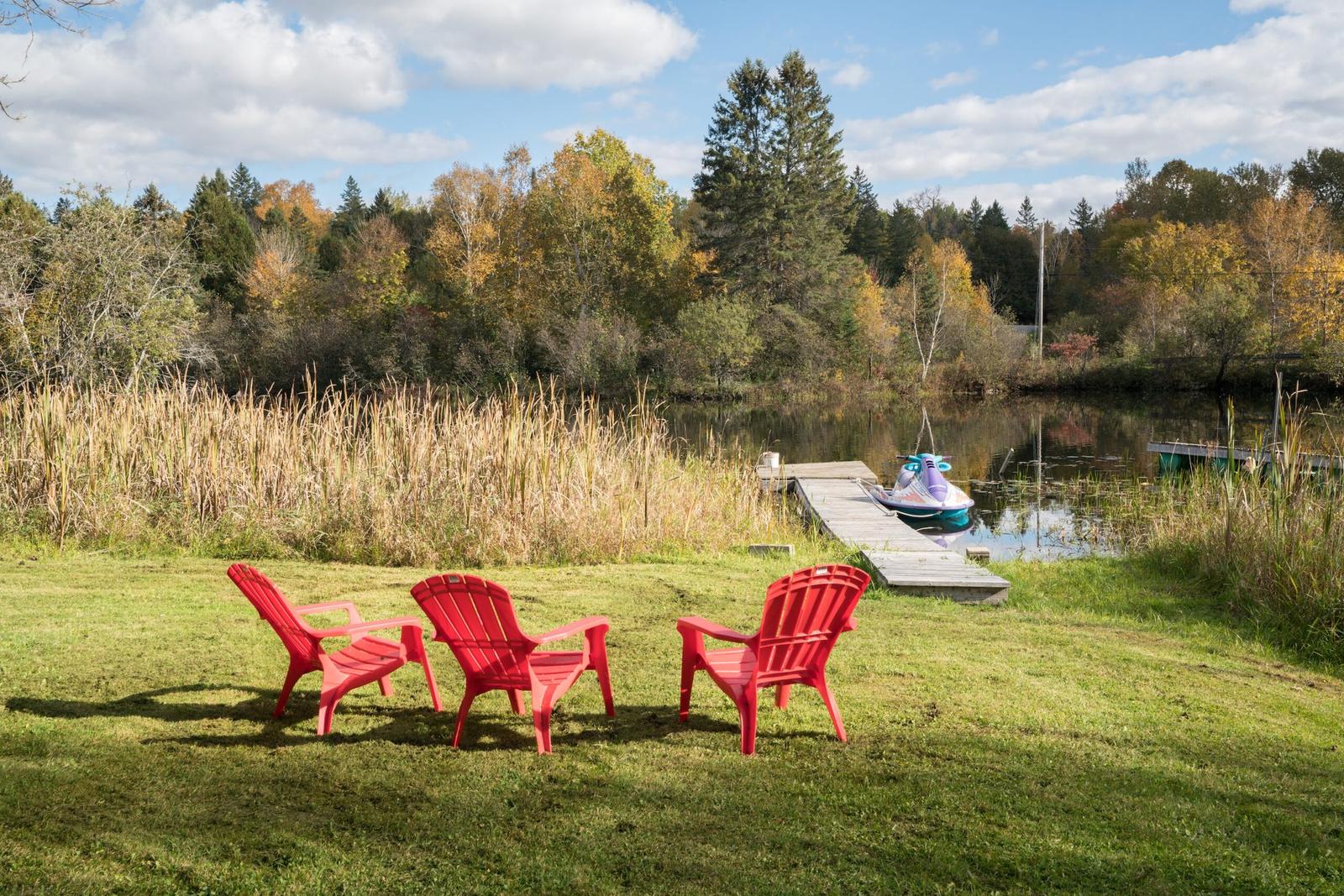 Red Adirondack chairs on the lawn beside the dock on Lac Long, Blue Sea