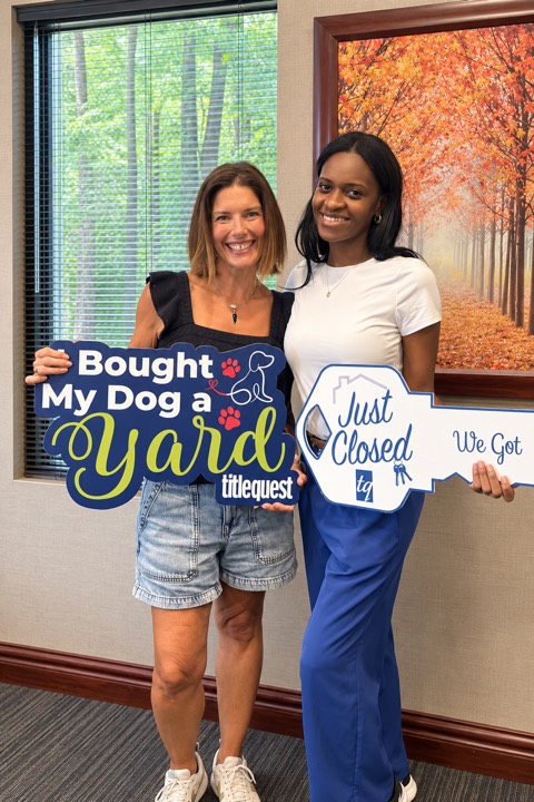 Two women celebrating a closing with Bought My Dog a Yard and Just Closed signs.