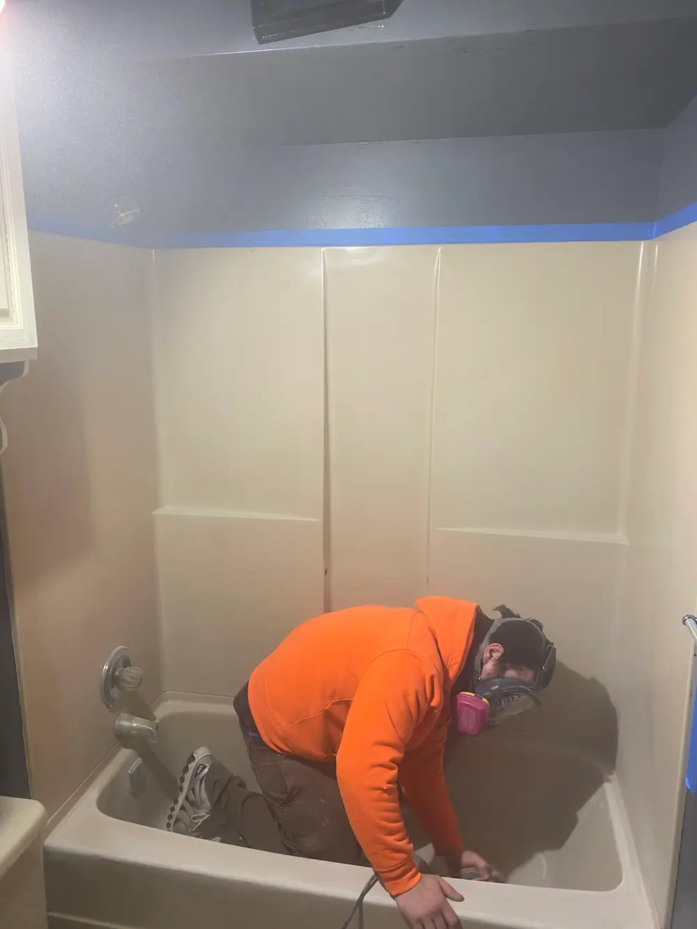 Reglaze Pro technician in respirator prepping a tub and surround for coating