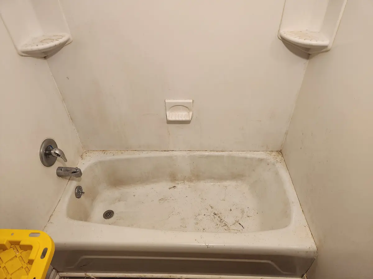 Soiled bathtub and surround with corner shelves before refinishing in an Ohio rental