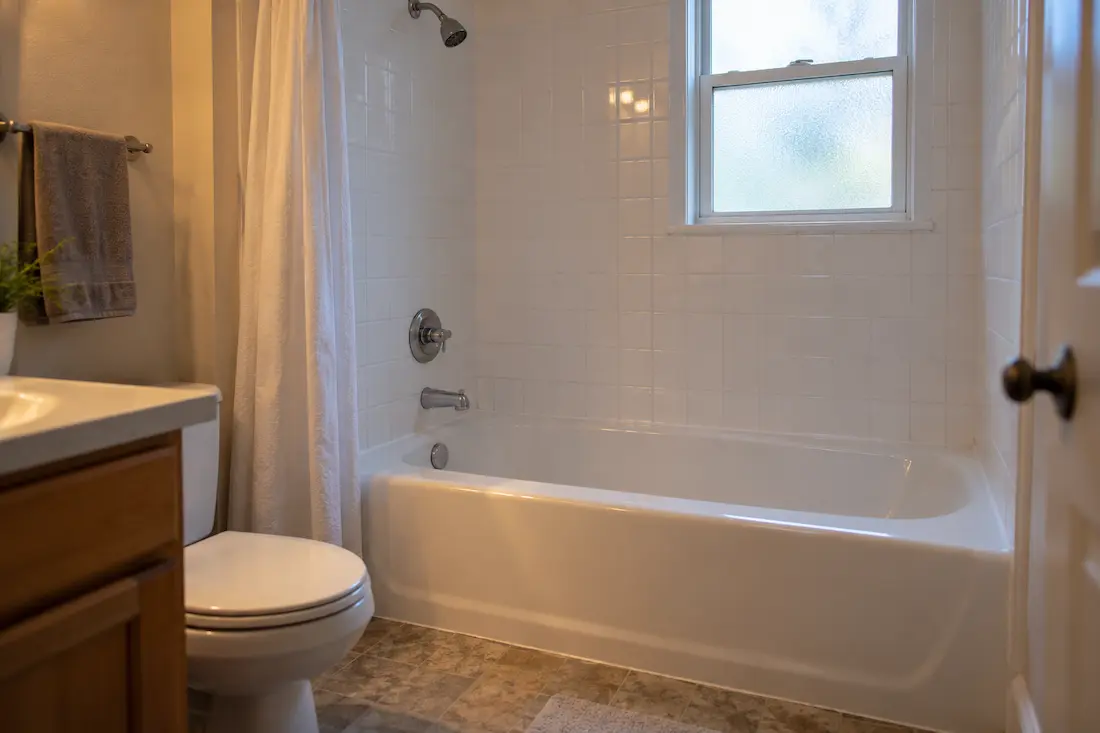 Rental apartment bathroom with a glossy white refinished alcove bathtub and plain white tile, typical of campus-area units in Bowling Green