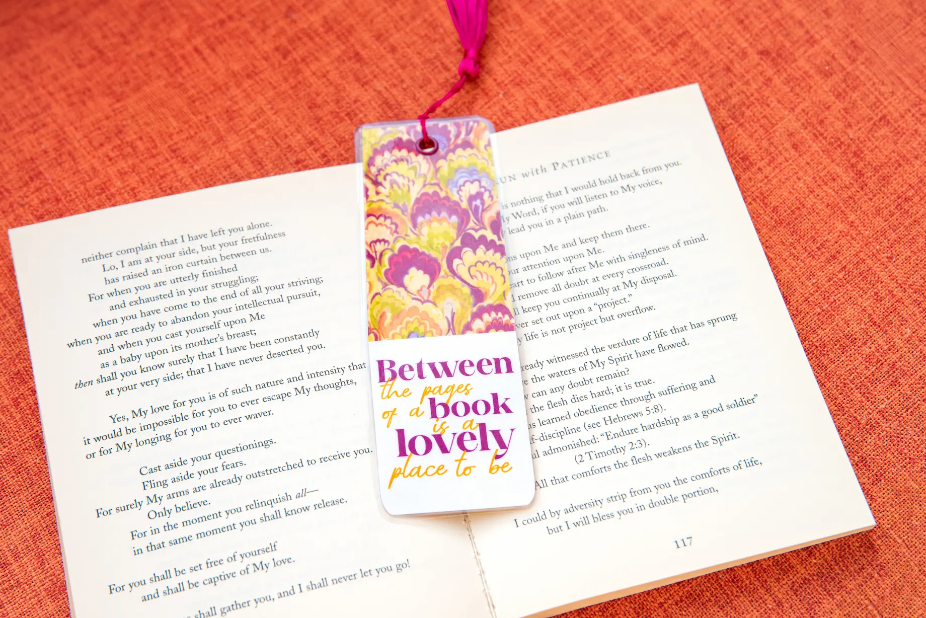 Double-sided laminated bookmark with a pink tassel resting on an open book