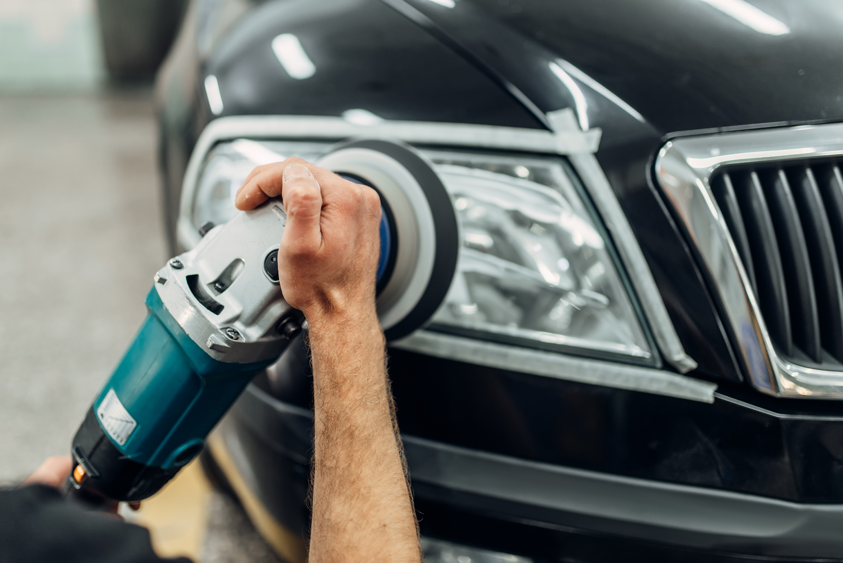 A person restoring headlights with a buffer tool.