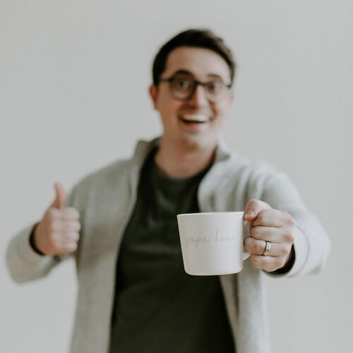 A man holding a cup of coffee and giving a thumbs up