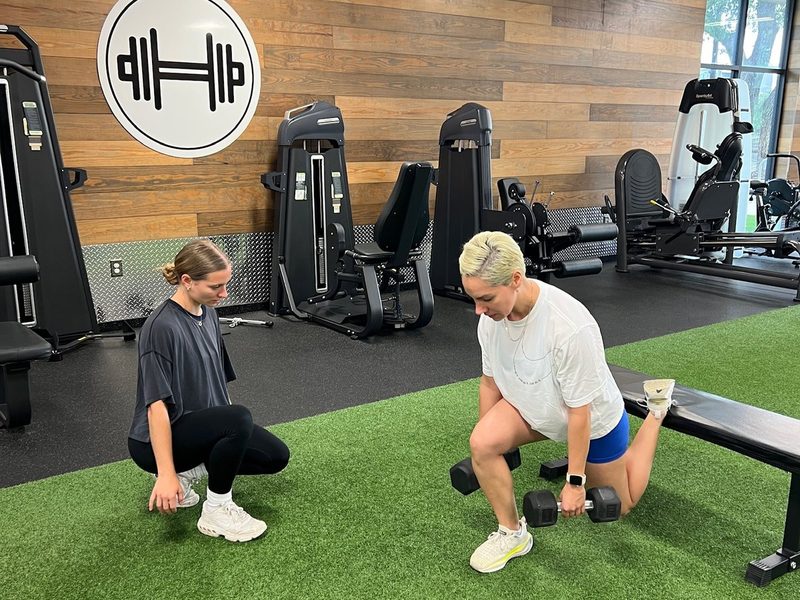 Personal trainer coaching a client through dumbbell lunges on the turf