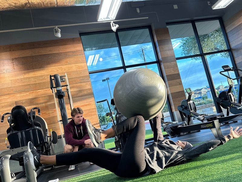 Client working through a stability ball core exercise on the turf with a coach watching form