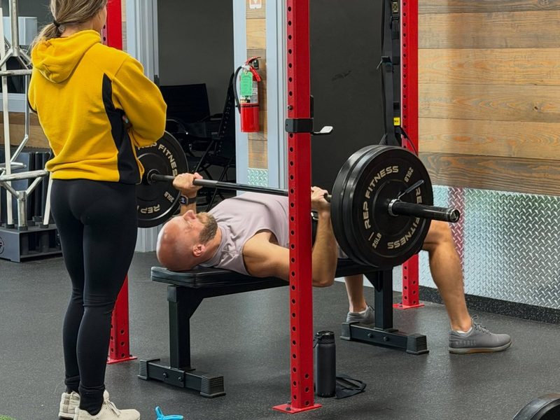 Personal trainer spotting a client through a barbell bench press in the squat rack